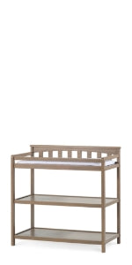 The Child Craft Flat Top Baby Changing Table in Dusty Heather features two open storage shelves and a raised edge for securing a changing pad, shown against a white background.