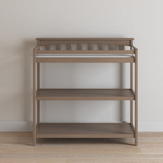 The Child Craft Flat Top Baby Changing Table in Dusty Heather features baby-safe finishes, two open shelves for nursery storage, and a top rail, shown against a white wall on a light wood floor.
