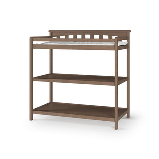 The Child Craft Flat Top Baby Changing Table in Dusty Heather features a medium brown wood tone, raised back and sides, a cushioned changing pad on top, and two open shelves below for nursery storage.