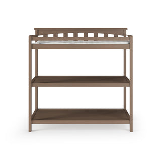 The Child Craft Flat Top Baby Changing Table in Dusty Heather features two open nursery storage shelves and a lattice-style back rail, shown with a baby changing pad against a white background.