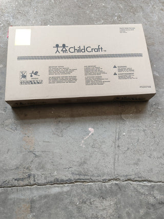 A sealed cardboard box labeled Child Craft rests on a concrete floor. It holds a Flat Top Baby Changing Table in cool gray, with safety warnings, product info, and a child-inspired logo—ideal for nursery or organizing changing table essentials.