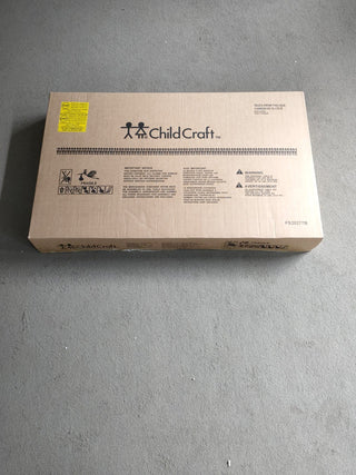 A rectangular cardboard box labeled Child Craft rests on a gray carpet, displaying icons and assembly instructions for the Arch Top Baby Changing Table in Matte White—an essential piece of nursery furniture.