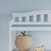 The Child Craft Arch Top Baby Changing Table in matte white stands against a pale blue wall, complementing nursery decor. A wicker apple-shaped basket and a wooden toy rest beside and under the table.