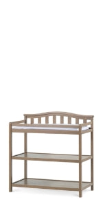 The Child Craft Arch Top Baby Changing Table in Dusty Heather features a raised back and sides, two open shelves for storage, and a stylish neutral finish, making it a practical and attractive addition to any nursery.