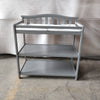 The Child Craft Arch Top Baby Changing Table in Cool Gray features a slatted back, two open shelves, and a padded changing mat, shown on a concrete floor against a neutral fabric backdrop.