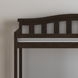The Child Craft Arch Top Baby Changing Table in Slate features a sleek, dark wood design and pairs perfectly with a slatted bench and light cushion, creating a stylish look against a plain light-colored nursery wall.
