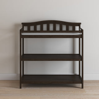 The Child Craft Arch Top Baby Changing Table in Slate features three open shelves and a slatted back and sides, offering simple, functional nursery storage. Its dark finish stands out against light walls and wooden floors—perfect for any home.