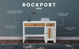 The Child Craft Rockport Desk - Sandstone features two drawers, a cabinet, dark metal pulls, rustic wood texture, and subtle tapered feet, shown with a black lamp on top against a blue wall and wooden floor with a patterned rug.