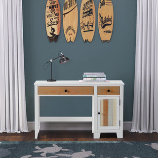 The Child Craft Rockport Desk in Sandstone, featuring a drawer and cabinet, stands against a teal wall with books and a black lamp on top. Four surfboards hang above; white curtains surround, and a blue patterned rug lies below.