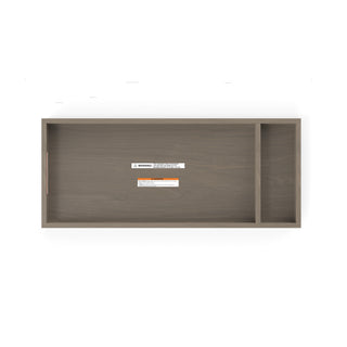 Child Craft F01792 Universal Dressing Kit in Crescent Grey: rectangular wooden topper with two compartments (large and small), viewed from above. Warning/info labels inside larger compartment; surface has a light brown wood grain finish.