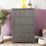 The Child Craft Atwood 4-Drawer Chest in Lunar Gray stands against a two-tone wall with giraffe wallpaper. On top are a giraffe print, books, and a small plant; baskets and another potted plant sit nearby on the floor.