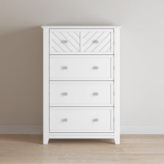 The Child Craft Atwood 4-Drawer Chest in matte white features a geometric-patterned top drawer and stands against a light beige wall on a wood floor.