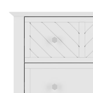 The image shows the upper left corner of the Child Craft Atwood 4-Drawer Chest in matte white, featuring diagonal paneling and two visible hexagonal knobs on the drawers.