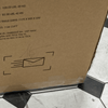 A brown box on a black-and-white tiled floor displays shipping details—weight, dimensions, and origin—for the Child Craft Atwood 4-in-1 Convertible Crib in Lunar Gray, with an envelope icon and a shipping compliance note.