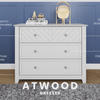 The Child Craft Atwood 3-Drawer Dresser in Matte White features a chevron pattern, beveled edges, three spacious drawers with hexagonal pulls. Shown with decor on top, blue paneled wall and gray rug; product name is labeled below.