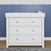 The Child Craft Atwood 3-Drawer Dresser in matte white stands by a blue paneled wall, with a gray rug in front and a pink soap dispenser on top.