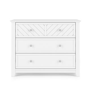 The Child Craft Atwood 3-Drawer Dresser in matte white features geometric patterns on the top drawer and round knobs, set against a white background.
