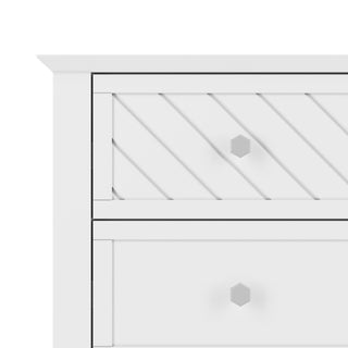 The Child Craft Atwood 3-Drawer Dresser in Matte White features geometric handles, a top drawer with diagonal grooves, and a smooth lower drawer. Only the upper left corner of the dresser is shown.