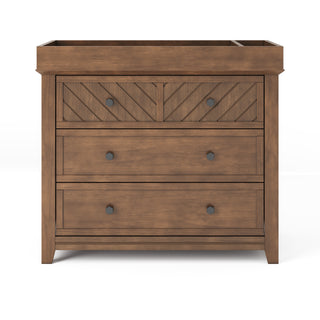 The Child Craft Atwood 3-Drawer Dresser in Cocoa Bean features a chevron-patterned top drawer with two round knobs and two larger lower drawers, each with two round knobs and a smooth finish.