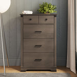 The Child Craft Redmond 4 Drawer Chest in Dapper Gray features two small and two large drawers with black handles. A green potted plant and books sit on top, and the chest stands against a gray paneled wall.