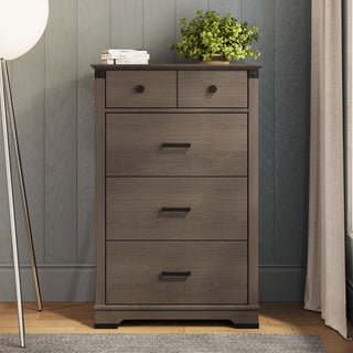 The Child Craft Redmond 4 Drawer Chest in Dapper Gray features two small and two large drawers with black handles. A green potted plant and books sit on top, and the chest stands against a gray paneled wall.