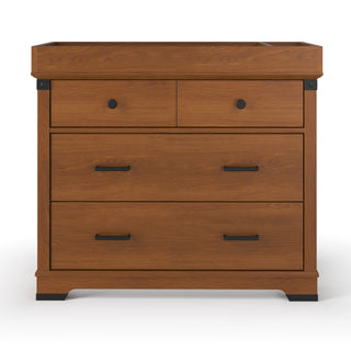 The Child Craft Redmond 3 Drawer Dresser in Coach Cherry features two small upper drawers with round black knobs, a large lower drawer with black handles, a honey-brown cherry finish, and a raised edge on the top surface.