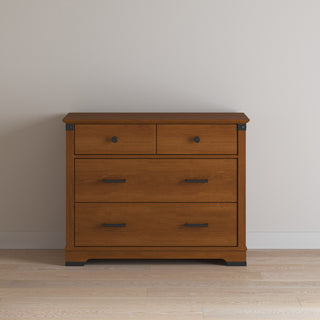 The Child Craft Redmond 3 Drawer Dresser in Coach Cherry has two small upper drawers and a larger lower drawer with black metal handles, set against a light wall on a wooden floor.