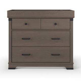 The Child Craft Redmond 3 Drawer Dresser in Dapper Gray features two small top drawers with round black knobs, a large lower drawer with a black handle, and raised edges on the top to help keep items secure.