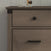 A close-up of the Child Craft Redmond 3 Drawer Dresser in Dapper Gray shows distinctive black hardware, with glass containers partially visible on top of this stylish nursery dresser.