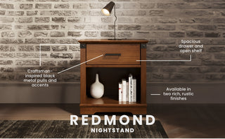 The Child Craft Redmond Nightstand in Coach Cherry features a spacious drawer, open shelf for books or decor, and black metal accents. Its charming finish and versatility make it a perfect nursery nightstand, beautifully highlighted against a brick wall.