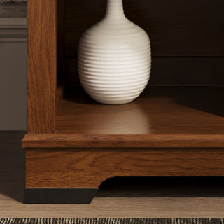 A white ribbed ceramic vase sits on the Child Craft Redmond Nightstand in Coach Cherry, with a dark brown finish. A glimpse of rug and wall nearby makes it a charming addition to any nursery or cozy corner.