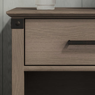 A close-up of the Child Craft Redmond Nightstand in Dapper Gray shows its drawer with a black handle, open shelf, and metal corner accents. A ribbed white object rests partially on top.