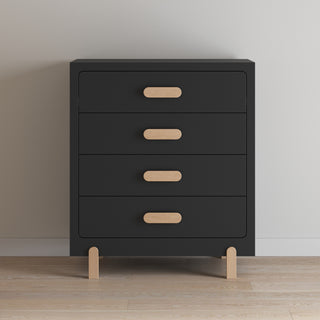 The Child Craft Park Heights 4-Drawer Chest in Caviar Black features sleek light wood handles and legs, combining modern style and ample storage, and stands elegantly against a white wall on a wooden floor.