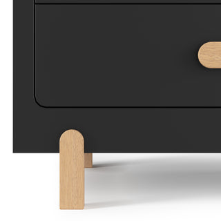 Close-up of the Child Craft Park Heights 4-Drawer Chest in Caviar Black, crafted from Brazilian hardwood with a rounded drawer, curved wooden handle, and light wood legs—an ideal minimalistic piece for modern bedrooms.