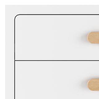 Close-up of the top left corner of the Child Craft Park Heights 4-Drawer Chest in Matte White, featuring sleek light wood handles. Its minimal design with Brazilian hardwood-inspired accents suits contemporary spaces perfectly.