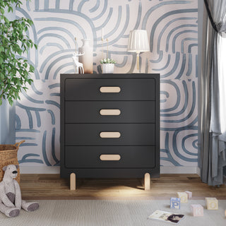 A modern nursery with the Child Craft Park Heights 4-Drawer Chest in Caviar Black, featuring wooden handles and legs, topped with a lamp, toys, and decor. Blue and white wavy wallpaper, a plush bear, and alphabet blocks complete the cozy look.