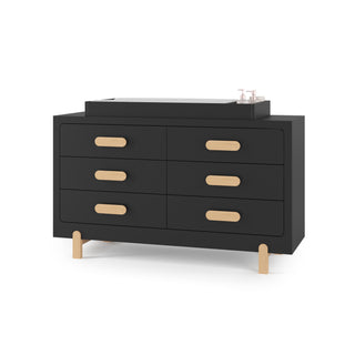 The Child Craft Legacy Changing Table Topper in Caviar Black sits on a modern black dresser with six drawers, light wood handles, and four light wood legs. Two bottles rest on the diaper changing surface.