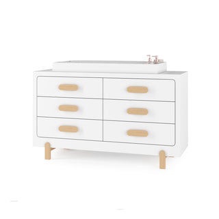 The Child Craft Legacy Changing Table Topper in Matte White sits atop a modern double dresser with six drawers, light wood handles and legs, and features copper-colored pump bottles.