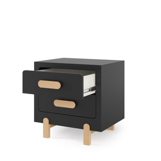 The Park Heights Night Stand - Caviar Black by Child Craft features light Brazilian hardwood legs and handles. Its open top drawer displays a stack of white papers or notebooks inside.