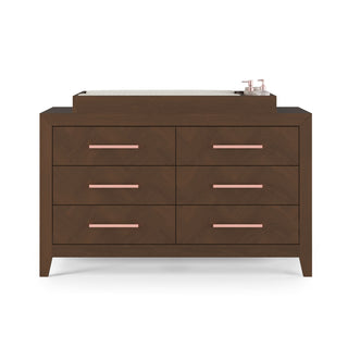 The Child Craft F01792 Universal Dressing Kit in Toasted Chestnut features a modern six-drawer wooden dresser with pink handles, topped with a changing pad and containers, all displayed against a plain white background.