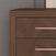 Close-up of the Child Craft Kieran 6-Drawer Double Dresser in Toasted Chestnut, showcasing its herringbone pattern and sleek metallic handles, set against a gray textured wall.
