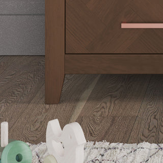 Close-up of the Child Craft Kieran 6-Drawer Double Dresser in Toasted Chestnut, featuring a copper handle, set on wooden flooring with part of a white textured rug and scattered wooden toys in the foreground.