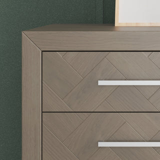 The Child Craft Kieran 6-Drawer Double Dresser in Crescent Gray features sleek horizontal metal handles and a herringbone pattern on its drawers, shown close-up against a dark green wall with part of a framed object on top.