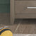 A plush toy with yellow and black stripes resembling a bee lies on a wooden floor next to the Child Craft Kieran 6-Drawer Double Dresser in Crescent Gray.