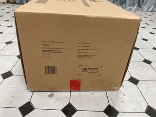 A large cardboard box labeled "Kieran 4-in-1 Convertible Crib, Toasted Chestnut" by Child Craft sits on a tiled floor, showing product details, barcodes, and a mail icon. A piece of red tape is near the bottom edge.