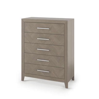The Child Craft Kieran 5-Drawer Chest in Crescent Gray features a modern, minimalist design with sleek silver handles, light brown wood finish, and short angled legs, perfect against a white backdrop.