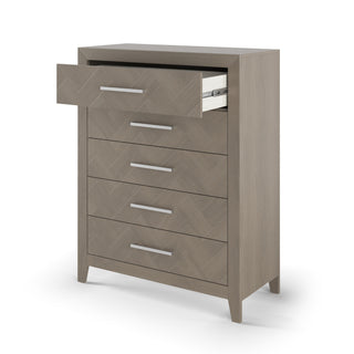 The Child Craft Kieran 5-Drawer Chest in Crescent Gray features five drawers with metal handles, angled legs, and a white interior visible in the open top drawer. Set against a plain white background.