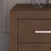 A close-up of the Child Craft Kieran Nightstand in Toasted Chestnut, featuring a geometric drawer pattern, metallic handle, and baby-safe finishes, with a decorative object on top and set against a textured wall.