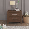 The Child Craft Kieran Nightstand in Toasted Chestnut with two drawers provides ample bedside storage against a gray paneled wall, topped with a lamp, books, and water. A nearby toy basket makes it ideal for a baby’s nursery.