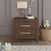 The Child Craft Kieran Nightstand in Toasted Chestnut with two drawers provides ample bedside storage against a gray paneled wall, topped with a lamp, books, and water. A nearby toy basket makes it ideal for a baby’s nursery.